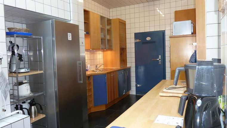 Eine moderne Küche mit weißen Fliesen und Holzschränken. Die Küchenausstattung umfasst einen Kühlschrank, einen Wasserkocher und eine Kaffeemaschine.