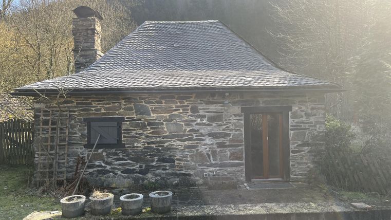 Ein kleines Steinhaus mit einem Satteldach und einer Holzveranda. Umgeben von Natur und Grün.