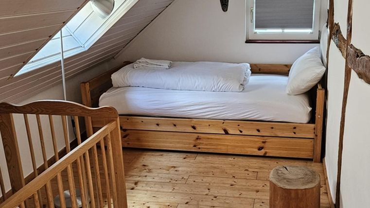 Ein gemütlicher Schlafzimmer mit einem Einzelbett und einem Kinderbett. Der Raum hat Holzfußboden und eine helle, einladende Atmosphäre.