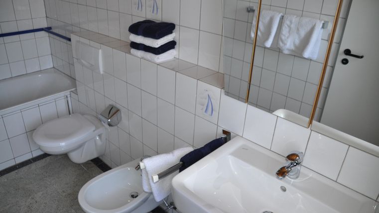 Ein modernes Badezimmer mit weißen Fliesen. Es sind Handtücher und Pflegeprodukte ordentlich arrangiert.