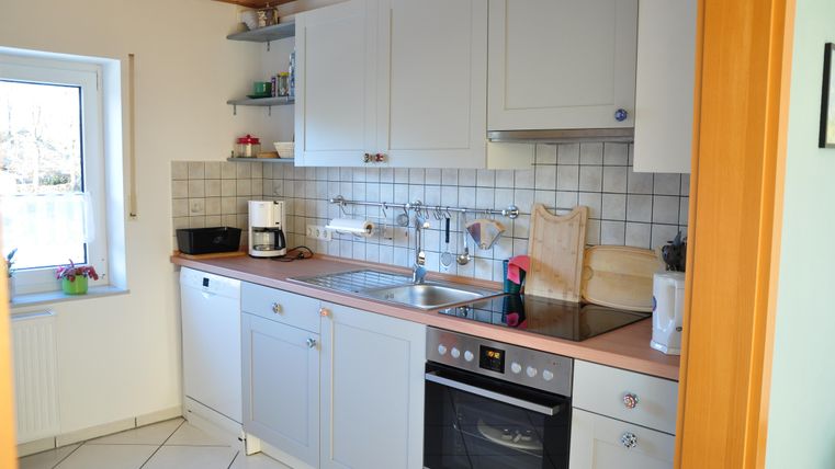 Eine helle, moderne Küche mit weißen Schränken und einem Fenster, das Tageslicht hereinlässt. Die Arbeitsfläche ist ordentlich und gut organisiert.