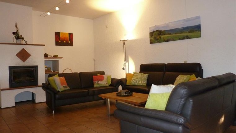 Ein modernes Wohnzimmer mit schwarzen Ledersofas und einem Holzkaffee Tisch. Die Wände sind hell, und es gibt Kunstwerke sowie einen Kamin.