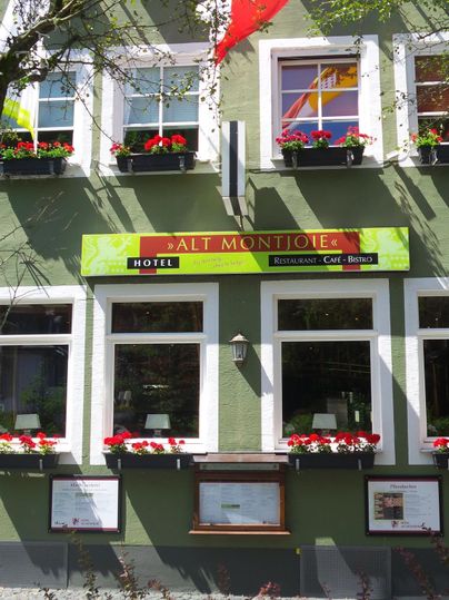 Ein einladendes Hotel mit bunten Blumenkästen und einem klaren, grünen Gebäude. Über dem Eingang weht eine deutsche Flagge.