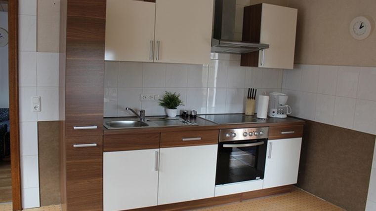 Moderne Küche mit Holz- und weißen Schränken. Sie ist sauber und gut ausgestattet mit einem Herd, Waschbecken und Küchenzubehör.