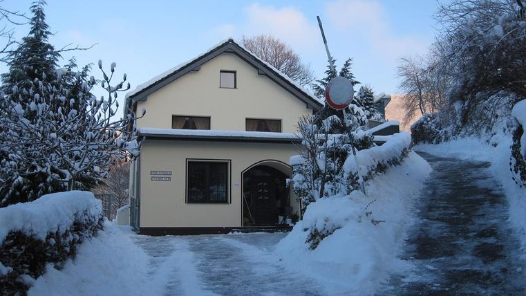 Ein charmantes Haus im Winter mit Schnee bedeckt. Der Weg zum Haus ist ebenfalls schneebedeckt und von Bäumen gesäumt.