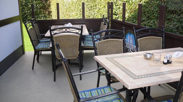 Ein gemütlicher Außenbereich mit Tischen und Stühlen. Die Atmosphäre ist einladend, umgeben von grünen Pflanzen.