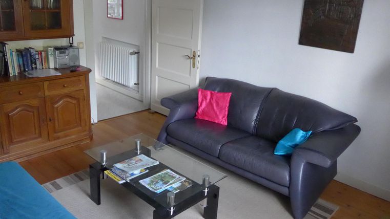 Ein gemütliches Wohnzimmer mit einem schwarzen Sofa und bunten Kissen. Ein Glastisch mit Zeitschriften steht davor.