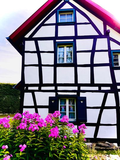 Ein traditionelles Fachwerkhaus mit weißen Wänden und schwarzen Balken. Vor dem Haus blühen bunte Blumen.