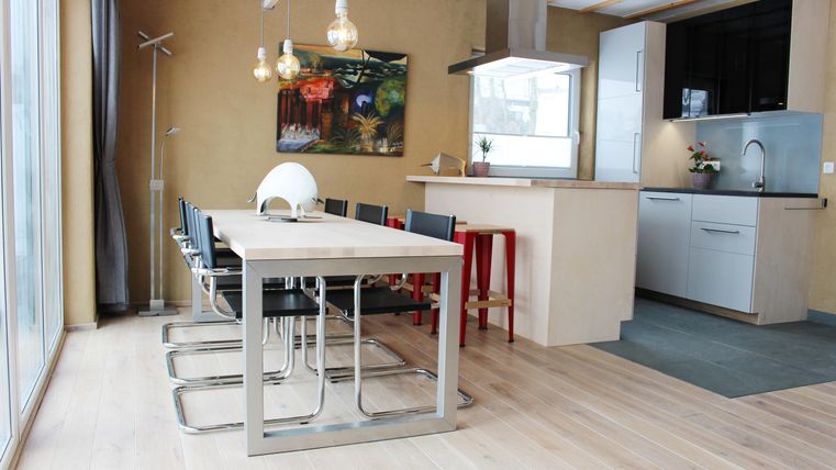 Ein modernes Esszimmer mit einem großen Tisch und schwarzen Stühlen. Die helle Küche ist offen und freundlich gestaltet.