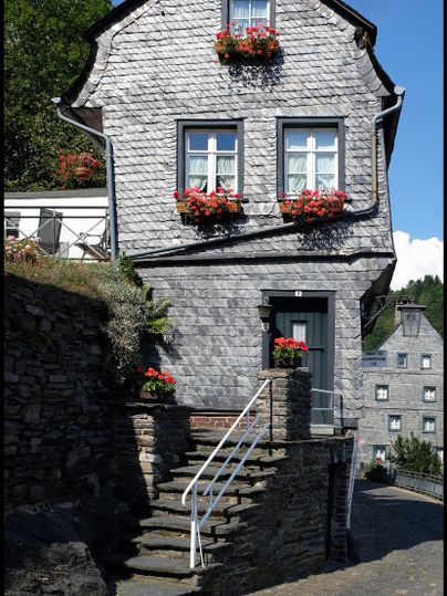 Ein charmantes Steinhaus mit blühenden Fensterkästen. Die Treppe führt zu einer einladenden Eingangstür.