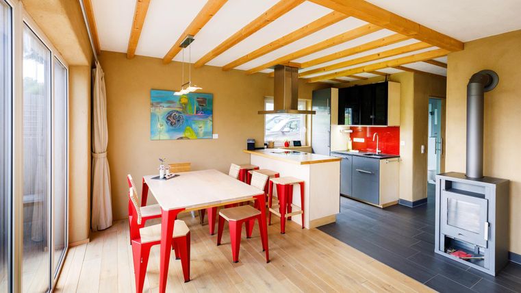 Eine moderne Küche mit einem großen Essbereich und roten Stühlen. Das Raumdesign ist hell und freundlich, mit Holzbalken an der Decke.