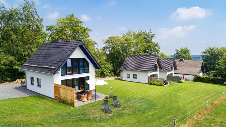 Verschiedene moderne Häuser stehen in einer grünen Landschaft. Der Himmel ist klar und sonnig, ideal für entspannende Tage im Freien.