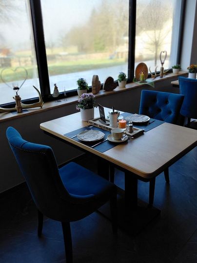 Ein gemütlicher Frühstückstisch in einem modernem Raum, dekoriert mit Pflanzen und Geschirr. Große Fenster bieten einen Blick ins Hohe Venn.