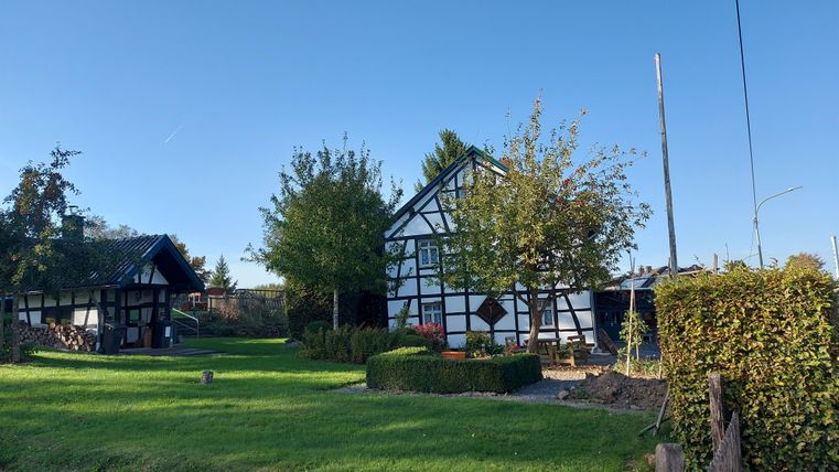 Ein hübsches, traditionelles Haus mit Fachwerk und einem großen Garten. Der Himmel ist klar und die Umgebung ist grün und einladend.