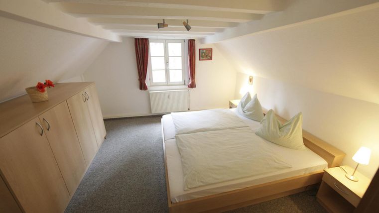 Ein gemütliches Schlafzimmer mit einem Doppelbett und Holzschränken. Helle Wände und sanftes Licht schaffen eine entspannte Atmosphäre.