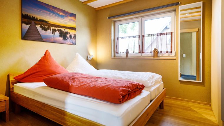 Ein gemütliches Schlafzimmer mit einem Doppelbett und bunten Kissen. An der Wand hängt ein schönes Landschaftsbild, und es gibt ein Fenster mit viel natürlichem Licht.