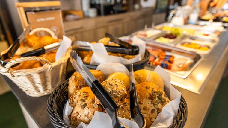 Ein Buffet mit frischen Brötchen in Körben. Im Hintergrund befinden sich verschiedene Speisen und Snacks.