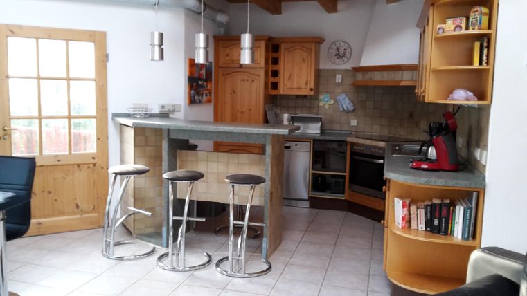 Eine moderne Küche mit Holzschränken und einer Bar mit Hockern. Das Design ist hell und freundlich, mit viel Platz für Aktivitäten.