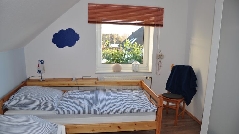 Ein gemütliches Schlafzimmer mit zwei Betten und blauen Streifenbettlaken. Das Fenster bietet einen Blick auf einen grünen Garten.