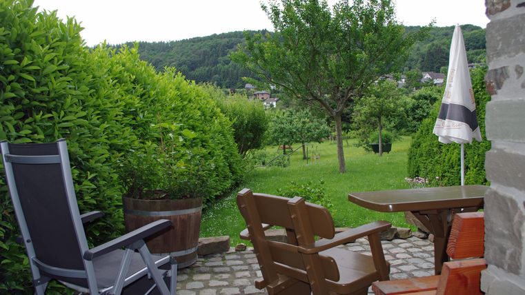 Ein gemütlicher Garten mit bequemen Stühlen und einem Tisch. Im Hintergrund sind Bäume und eine grüne Wiese zu sehen.