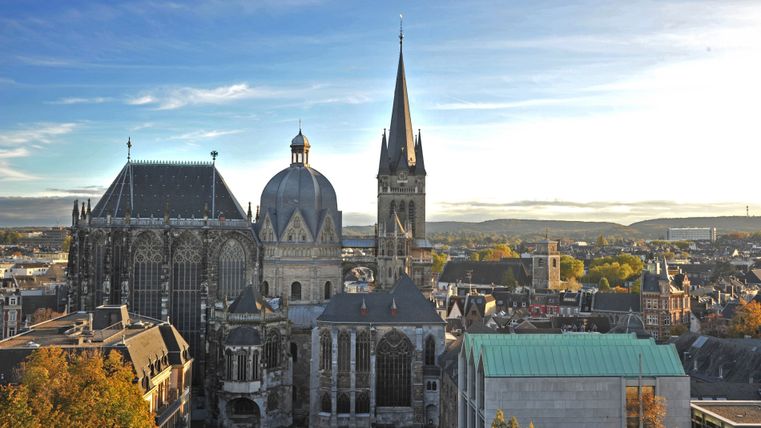 Panoramablick auf den Aachener Dom mit umliegender Stadtlandschaft bei Sonnenuntergang.