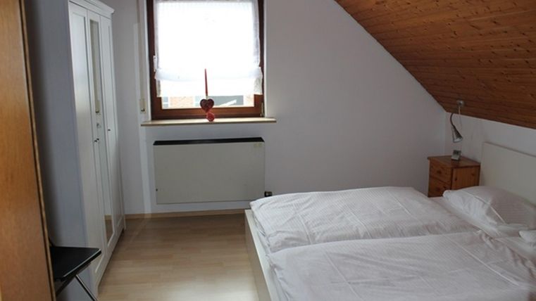 Ein einfaches Schlafzimmer mit zwei Einzelbetten und einem Fenster. Die Wände sind hell, und es gibt Möbel in Holzoptik.