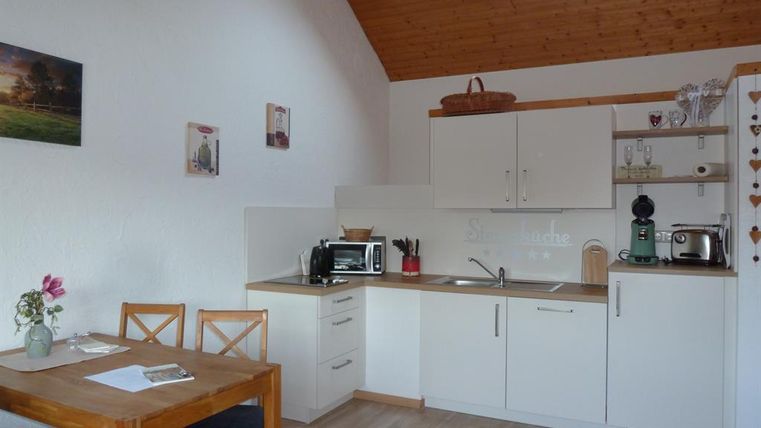 Eine moderne Küche mit Holzdecke und hellen Wänden. Es gibt einen Esstisch und verschiedene Küchengeräte.