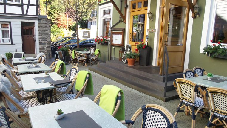 Ein einladendes Restaurant mit Tischen auf der Terrasse. Die Umgebung ist grün und freundlich, perfekt für eine Mahlzeit im Freien.