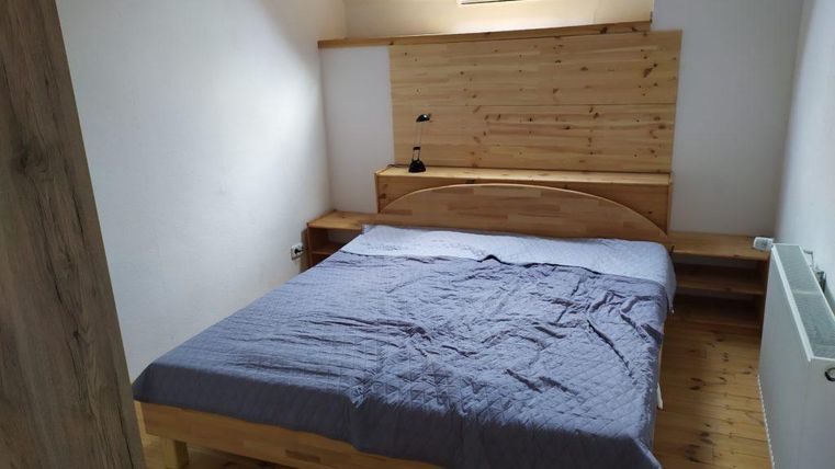 Ein einfaches Schlafzimmer mit einem Holzbett und einer blauen Bettdecke. Es gibt ein Fenster mit Dachfenster und eine Holzregalwand.