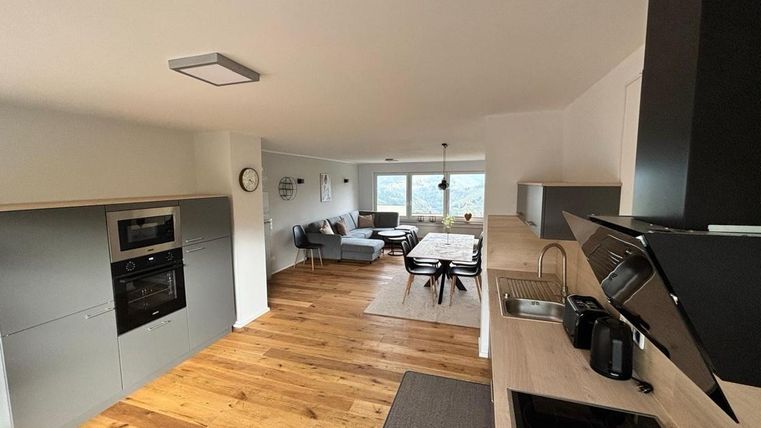 Eine moderne Küche mit Holzfußboden und eleganten Geräten. Im Hintergrund ist ein gemütlicher Wohnbereich mit einem Esstisch und einer schönen Aussicht zu sehen.
