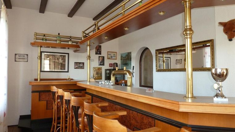 Eine gemütliche Bar mit hölzernen Barhockern und einem eleganten Bartresen. An den Wänden hängen Bilder und es gibt eine Trophäe auf dem Tresen.