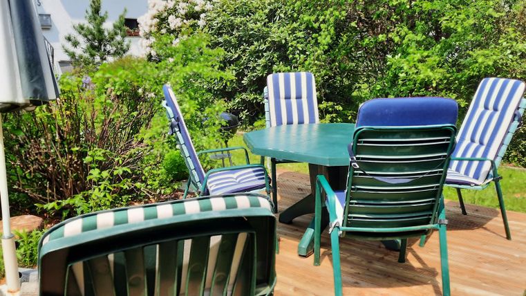 Ein einladender Sitzbereich im Garten mit einem runden Tisch und mehreren Stühlen. Umgeben von üppigem Grün und Pflanzen.