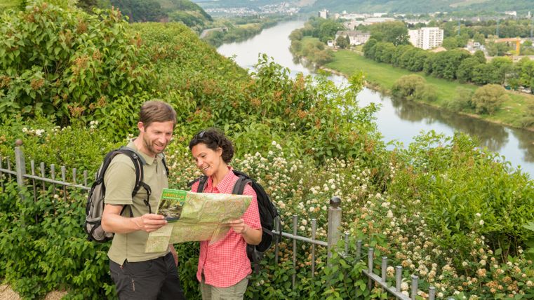 Zwei Wanderer betrachten eine Karte vor einer Flusslandschaft.