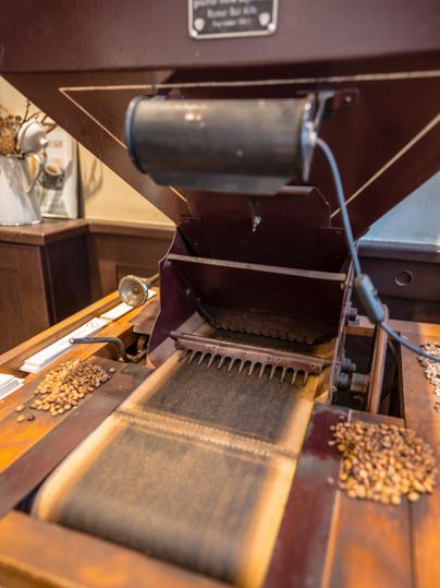Eine alte Kaffeemühle aus Holz mit einem integrierten Sieb. Kaffeebohnen liegen bereit, um verarbeitet zu werden.