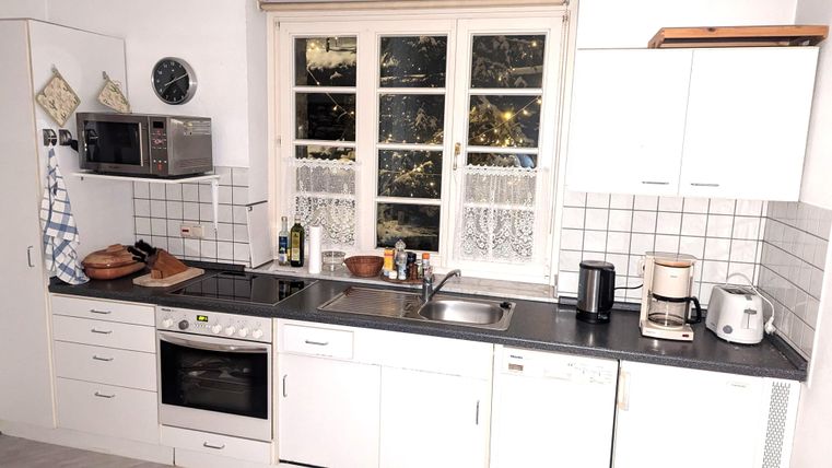 Eine moderne Küche mit weißen Schränken und einem Herd. Das Fenster bietet einen Blick nach draußen und ist mit einem Vorhang versehen.