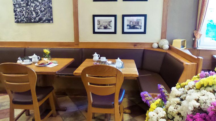 Ein gemütliches Café mit Holzmöbeln und Kaffee-Service auf einem Tisch. An der Wand hängen Bilder, und ein Blumenstrauß steht im Vordergrund.