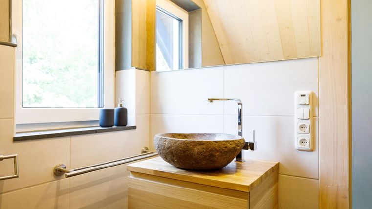 Ein modernes Badezimmer mit Holzdetails und einem runden Waschbecken. Das Fenster sorgt für viel natürliches Licht.