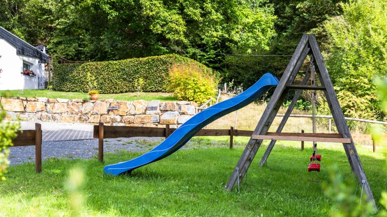 Eine Rutsche in einem grünen Garten mit Bäumen im Hintergrund. Der Spielplatz ist ruhig und einladend.
