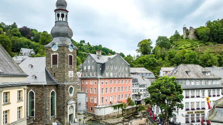 Blick auf die Altstadt von Monschau mit dem markanten Roten Haus und einer Kirche im Vordergrund.