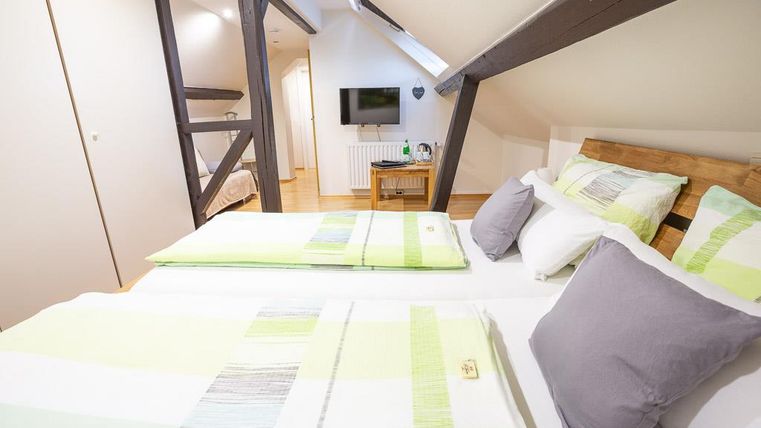 Ein gemütliches Schlafzimmer mit zwei Betten, die mit hellen, gestreiften Bettwäsche dekoriert sind. Die Holzdecke und der Fernseher im Hintergrund sorgen für ein einladendes Ambiente.