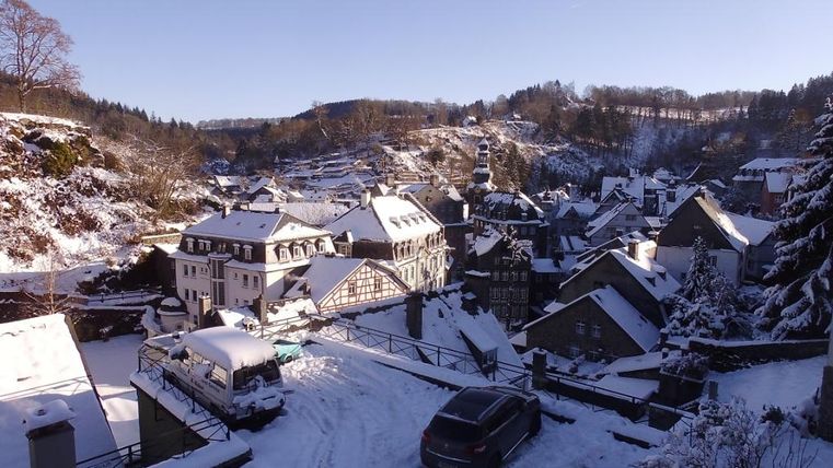 Eine verschneite Stadt mit charmanten Häusern und sanften Hügeln im Hintergrund. Der klare Himmel sorgt für eine ruhige Winteratmosphäre.