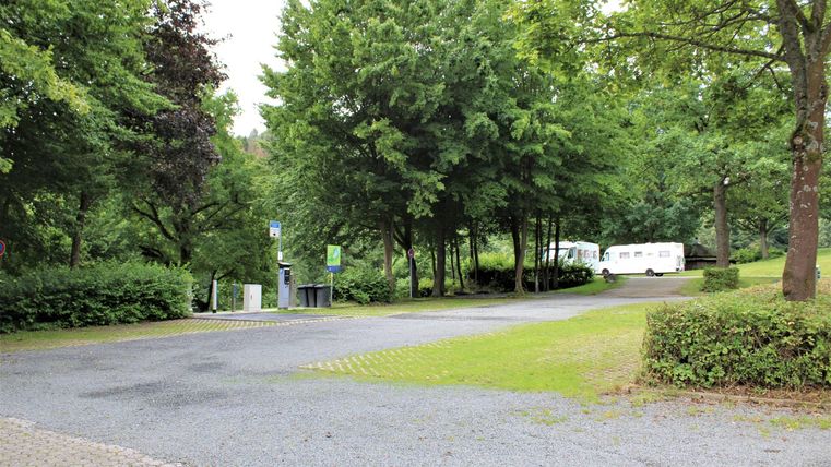 Eine ruhige Straße umgeben von Bäumen und Grünflächen. Im Hintergrund sind Wohnmobile zu sehen.