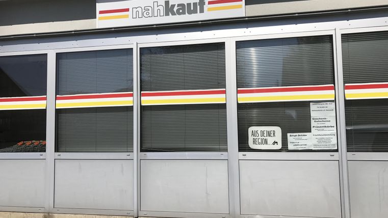 Ein Geschäft mit der Beschriftung "nahkauf" an der Wand. Die Fenster sind verglast und es gibt ein Schild, das auf regionale Produkte hinweist.