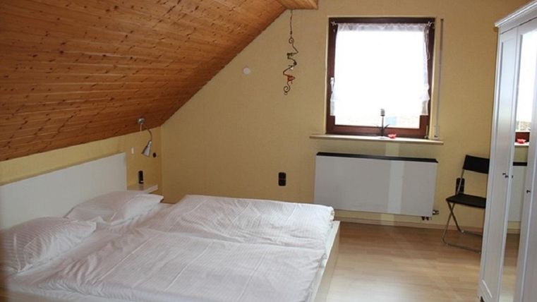 Ein gemütliches Schlafzimmer mit einem Doppelbett und einem Fenster. Die Wände sind in warmen Farben, und die Decke hat eine Holzvertäfelung.