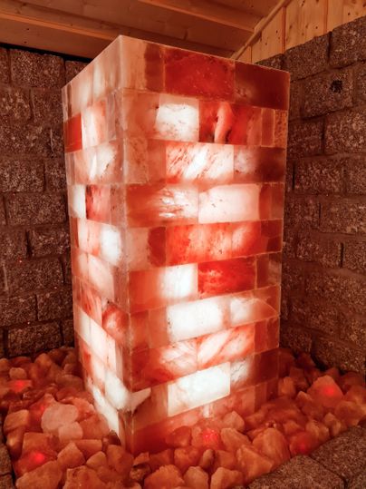 Ein großer Block aus pinkem Salz, der von innen beleuchtet ist. Rund um den Block liegen kleinere Salzstücke auf dem Boden.