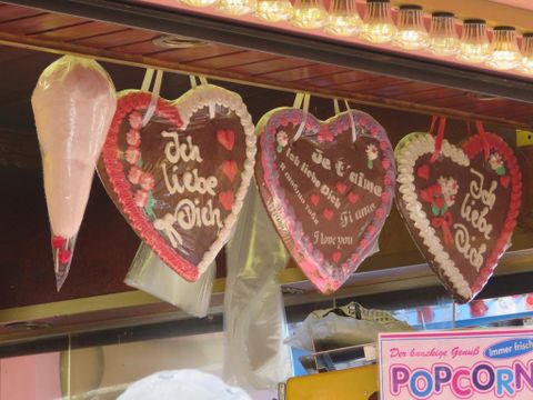Bunte Lebkuchenherzen mit romantischen Botschaften hängen an einem Stand. Rechts sieht man eine Tüte Zuckerwatte.