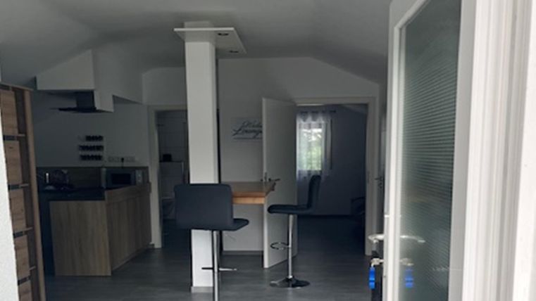 Eine moderne Küche mit Barhockern und hellem Interieur. Der Raum ist gut beleuchtet und freundlich gestaltet.