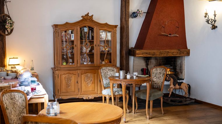 Ein gemütliches Esszimmer mit einem Holztisch und bequemen Stühlen. Im Hintergrund befindet sich ein Kamin und eine elegante Vitrine mit Geschirr.