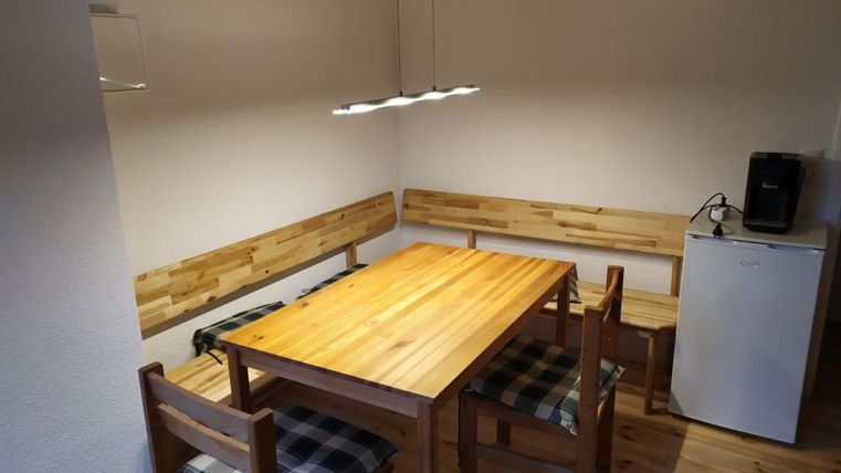 Ein gemütlicher Essbereich mit einem Holztisch und Stühlen. An einer Wand befinden sich Bänke und ein Kühlschrank in der Ecke.