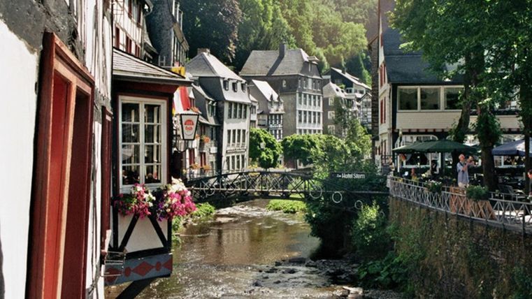 Eine malerische Stadt am Fluss mit hübschen Häusern und grünen Bäumen. Die Brücke verbindet die beiden Ufer und schafft eine charmante Atmosphäre.